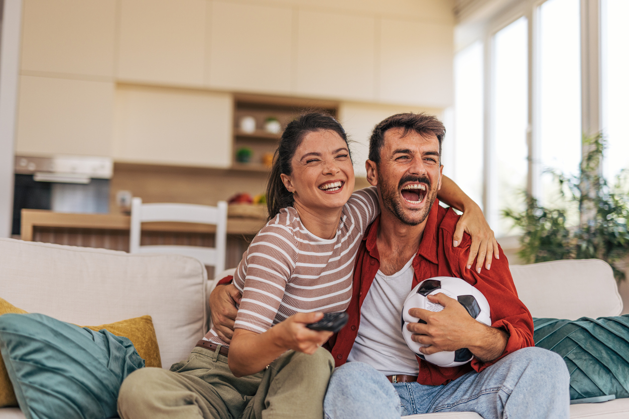 couple laughing and watching football match on tv at home